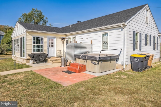 rear view of property with a hot tub, a lawn, and a patio area