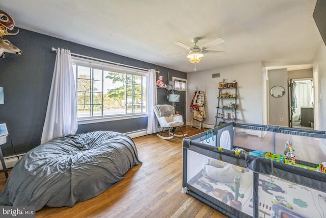 bedroom with ceiling fan, a baseboard heating unit, and light hardwood / wood-style floors