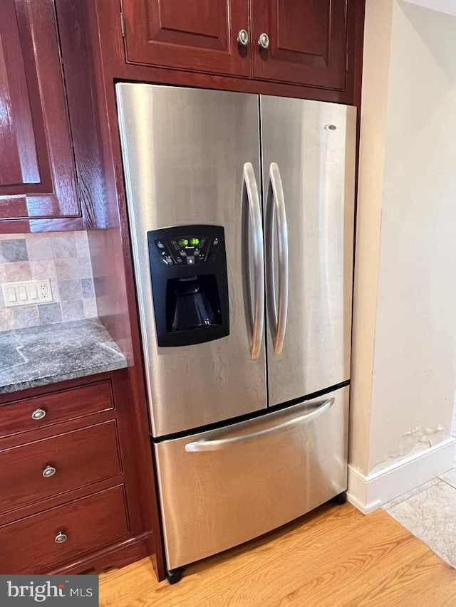 kitchen featuring decorative backsplash, stainless steel fridge with ice dispenser, dark stone counters, and light hardwood / wood-style flooring