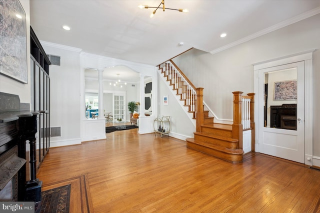 interior space featuring ornate columns, ornamental molding, a chandelier, and light hardwood / wood-style floors