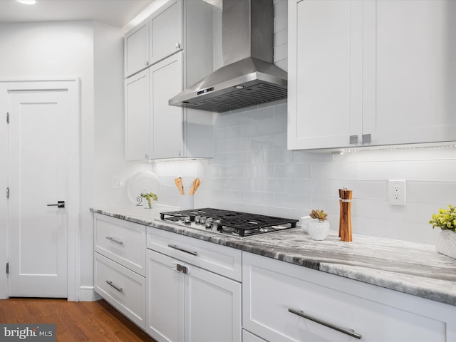 kitchen featuring dark wood-type flooring, white cabinets, wall chimney range hood, and stainless steel gas stovetop