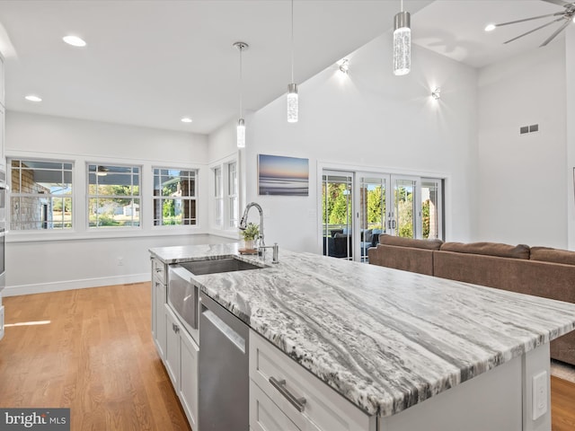 kitchen featuring light wood-type flooring, an island with sink, hanging light fixtures, white cabinetry, and stainless steel dishwasher