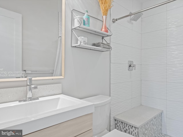 bathroom featuring vanity, a tile shower, and toilet