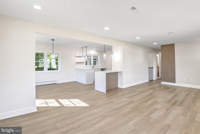 unfurnished living room with light hardwood / wood-style floors, sink, and a baseboard heating unit