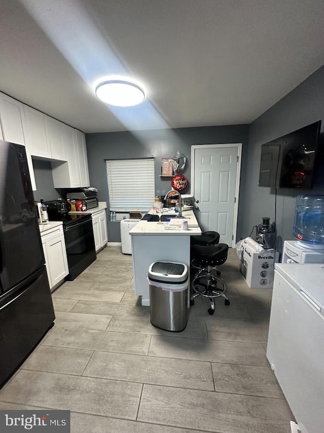 kitchen with a kitchen island with sink, white cabinetry, black appliances, a breakfast bar, and light wood-type flooring