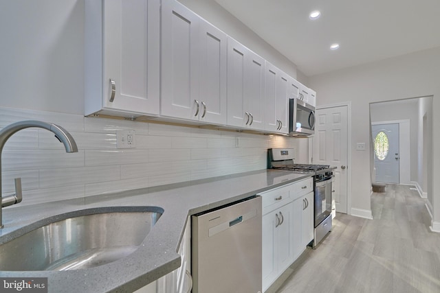 kitchen featuring decorative backsplash, appliances with stainless steel finishes, light stone counters, sink, and white cabinetry