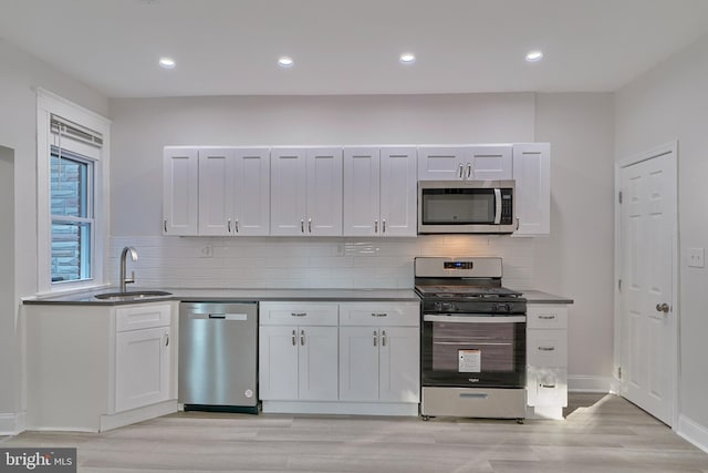 kitchen with white cabinets, sink, appliances with stainless steel finishes, tasteful backsplash, and light hardwood / wood-style floors