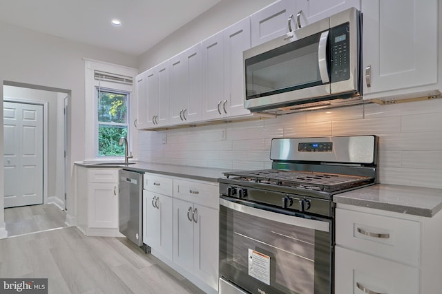 kitchen with white cabinetry, sink, appliances with stainless steel finishes, tasteful backsplash, and light hardwood / wood-style floors