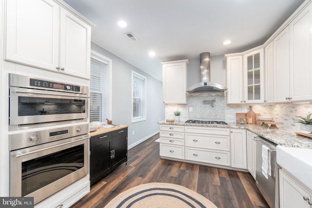 kitchen with appliances with stainless steel finishes, wall chimney exhaust hood, dark wood-type flooring, and white cabinetry