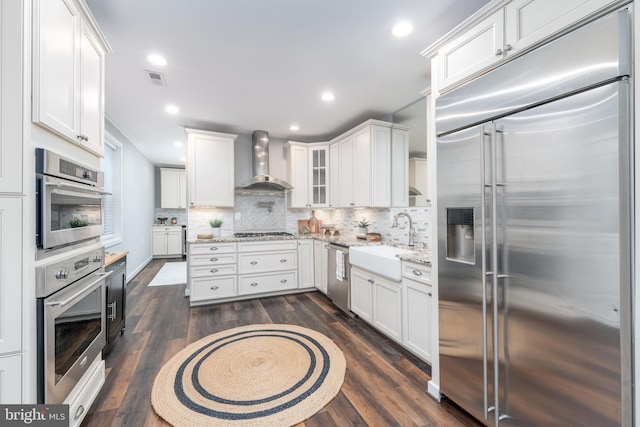 kitchen with stainless steel appliances, wall chimney exhaust hood, dark wood-type flooring, sink, and white cabinetry