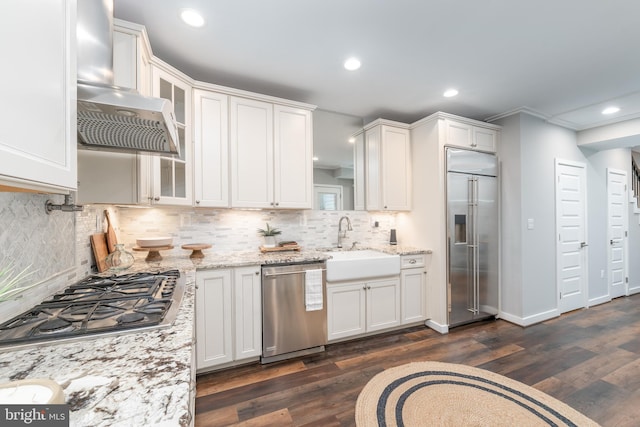 kitchen featuring appliances with stainless steel finishes, dark hardwood / wood-style flooring, wall chimney range hood, and white cabinetry