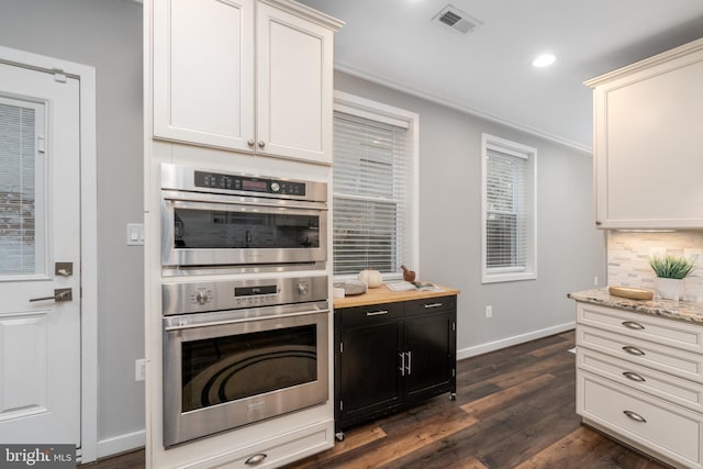 kitchen with double oven, light stone counters, white cabinets, and dark hardwood / wood-style flooring