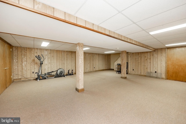 basement featuring wooden walls, a drop ceiling, and carpet