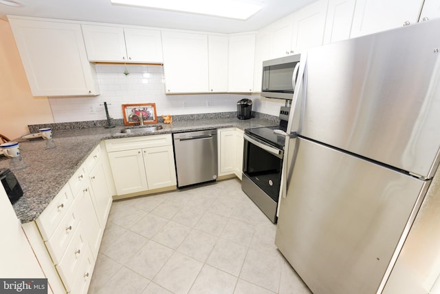 kitchen featuring light tile patterned flooring, white cabinets, dark stone counters, appliances with stainless steel finishes, and a sink