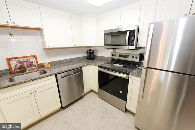 kitchen featuring light tile patterned floors, a sink, appliances with stainless steel finishes, white cabinetry, and backsplash