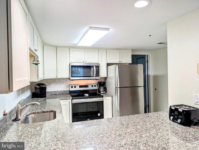 kitchen featuring white cabinets, appliances with stainless steel finishes, light stone counters, a sink, and backsplash