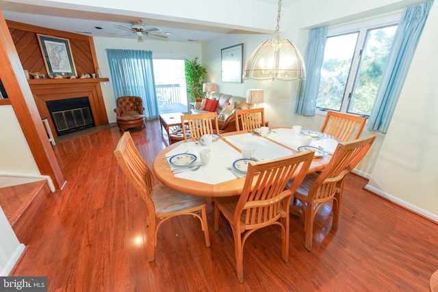 dining area featuring baseboards, ceiling fan, wood finished floors, and a fireplace with flush hearth