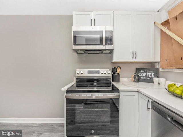 kitchen featuring white cabinets, stainless steel appliances, hardwood / wood-style flooring, and light stone counters