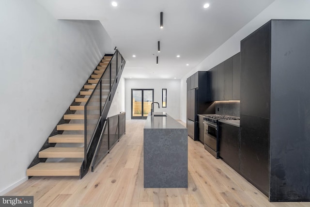 kitchen with sink, a kitchen island with sink, appliances with stainless steel finishes, and light hardwood / wood-style flooring