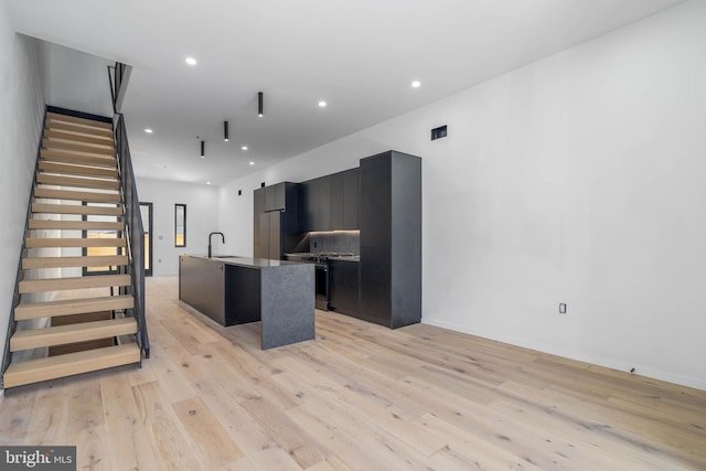 kitchen featuring sink, a kitchen island with sink, stainless steel range, and light hardwood / wood-style flooring