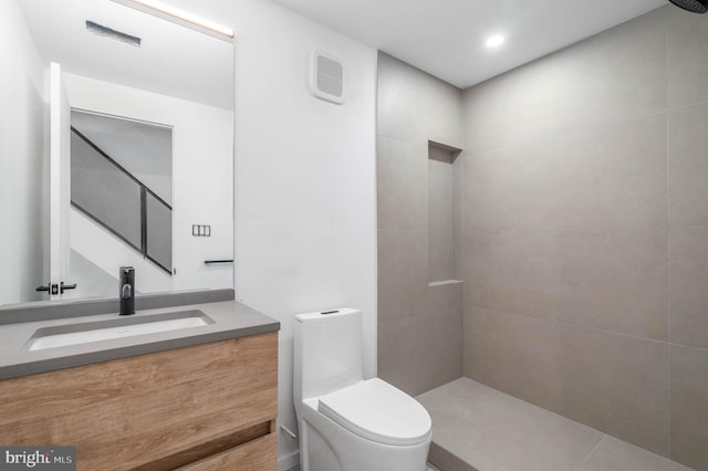 bathroom featuring a tile shower, tile patterned floors, vanity, and toilet