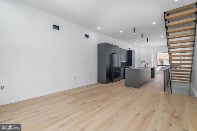 kitchen featuring sink, appliances with stainless steel finishes, light wood-type flooring, and an island with sink