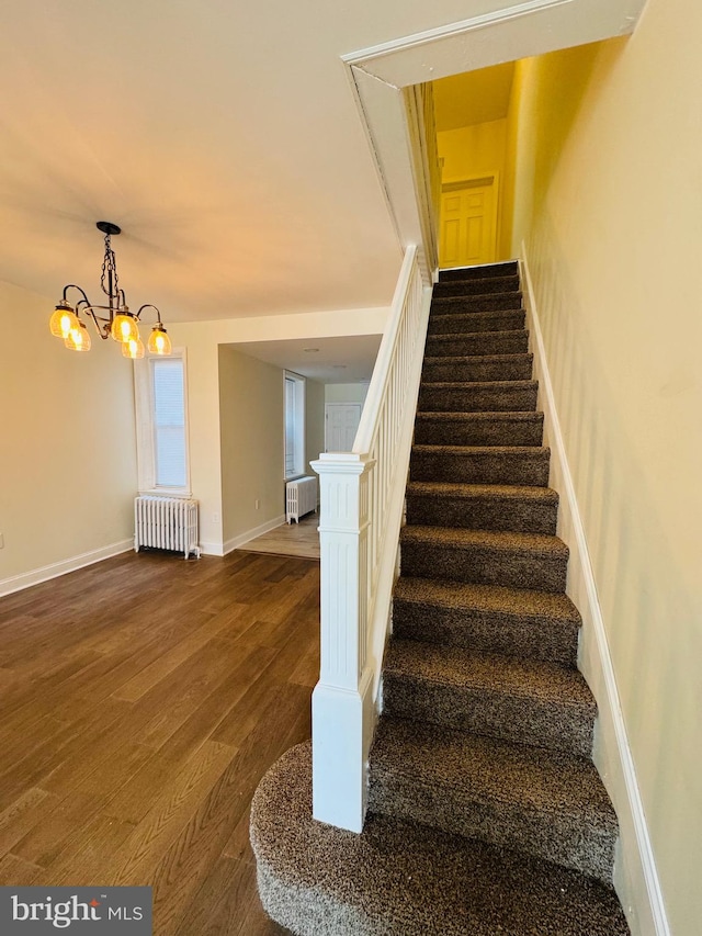 stairs with a notable chandelier, wood-type flooring, and radiator