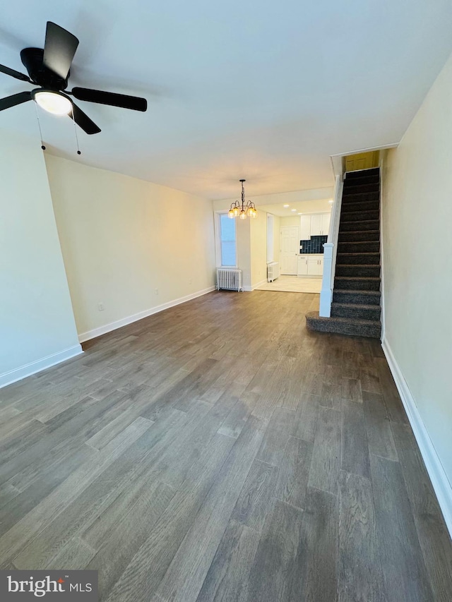 unfurnished living room with radiator heating unit, ceiling fan with notable chandelier, and dark hardwood / wood-style flooring