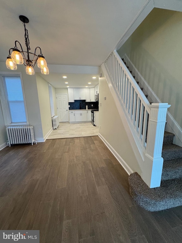 unfurnished living room featuring wood-type flooring, radiator heating unit, and a chandelier