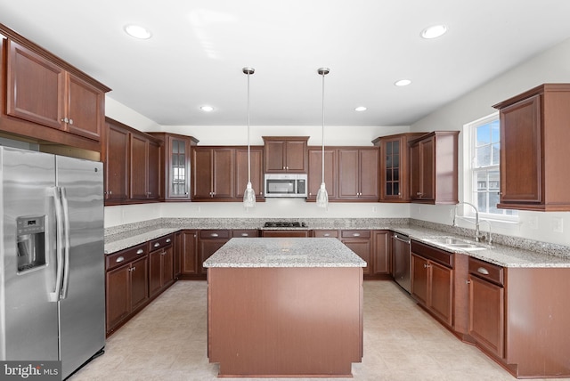 kitchen with hanging light fixtures, light stone countertops, stainless steel appliances, sink, and a center island