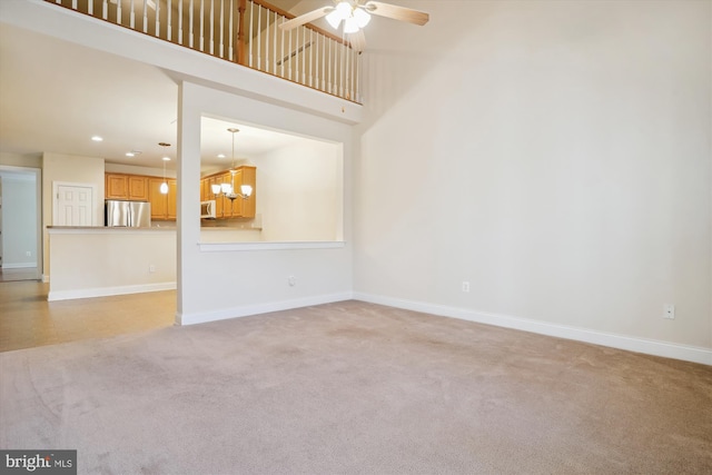 unfurnished living room with ceiling fan with notable chandelier, a towering ceiling, and light carpet