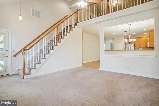 unfurnished living room featuring a towering ceiling, a notable chandelier, and light carpet