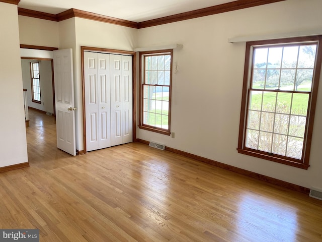 unfurnished bedroom featuring ornamental molding, multiple windows, a closet, and light hardwood / wood-style flooring