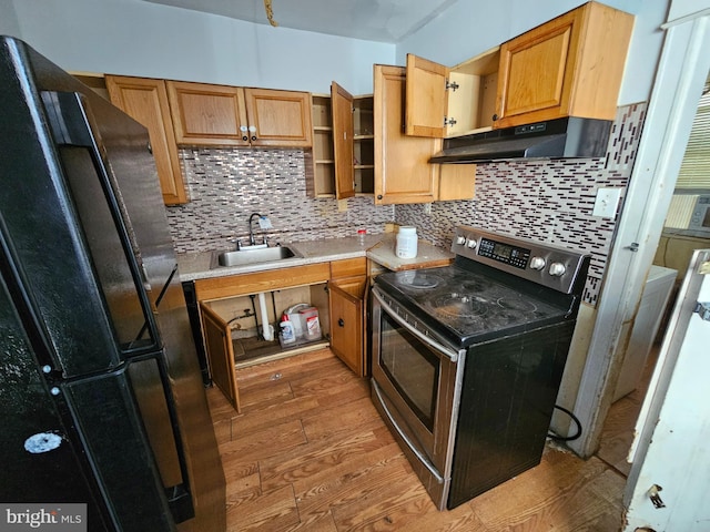 kitchen featuring light wood-type flooring, sink, stainless steel electric range oven, backsplash, and black refrigerator