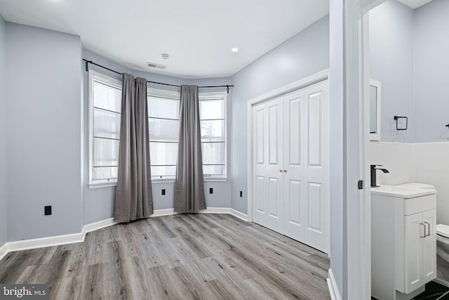 unfurnished bedroom featuring sink, a closet, multiple windows, and light wood-type flooring