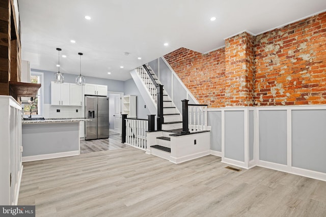 interior space featuring white cabinets, stainless steel refrigerator with ice dispenser, decorative light fixtures, and light wood-style flooring