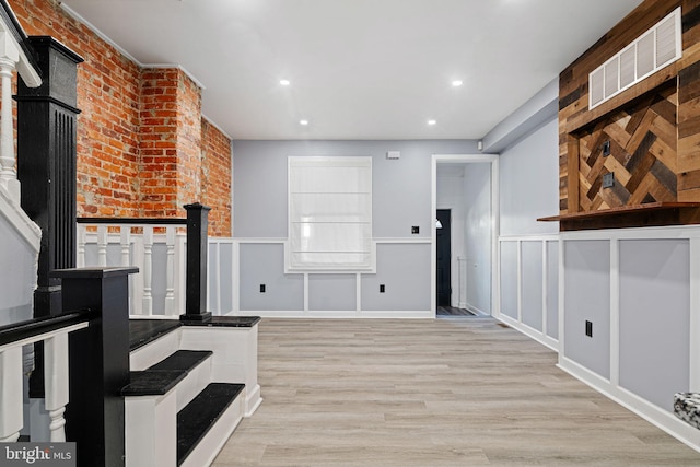 interior space featuring visible vents, a decorative wall, light wood-style flooring, and wainscoting