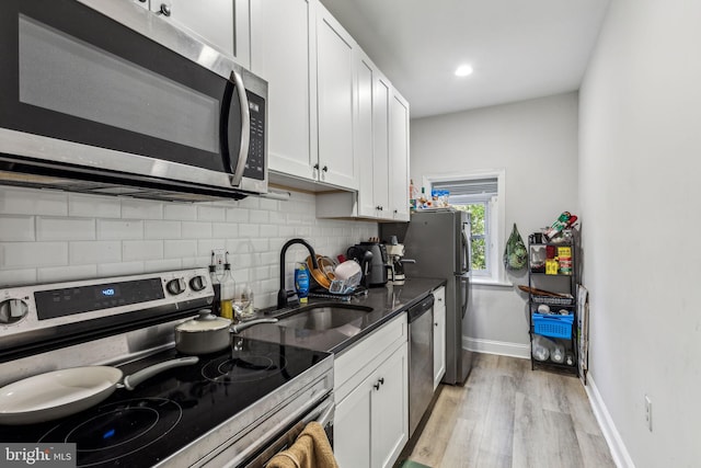 kitchen with backsplash, appliances with stainless steel finishes, sink, white cabinets, and light hardwood / wood-style flooring