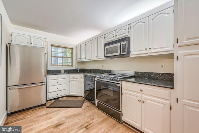 kitchen featuring sink, dark stone counters, white cabinetry, black appliances, and light wood-type flooring