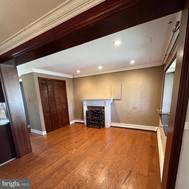 unfurnished living room featuring wood-type flooring, ornamental molding, and baseboard heating