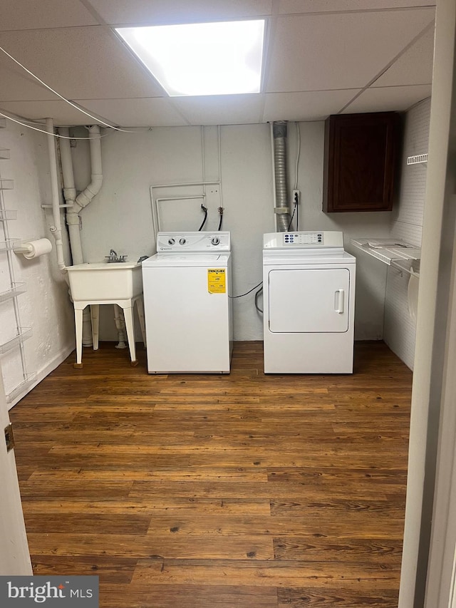 clothes washing area with washing machine and dryer, dark hardwood / wood-style floors, and cabinets