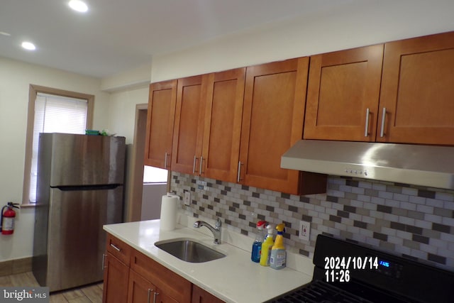 kitchen featuring stove, sink, decorative backsplash, stainless steel fridge, and light wood-type flooring