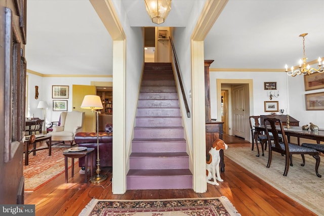 stairs featuring ornamental molding, hardwood / wood-style floors, and a notable chandelier