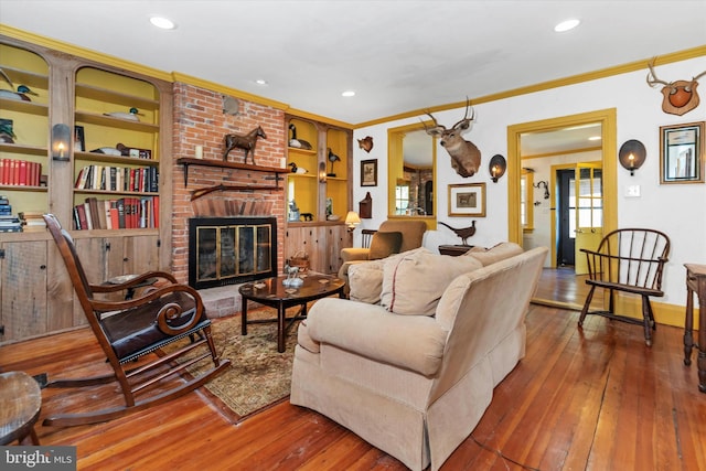 living room with crown molding, a brick fireplace, wood-type flooring, and built in features