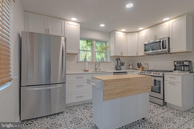 kitchen with wooden counters, sink, white cabinets, appliances with stainless steel finishes, and tasteful backsplash