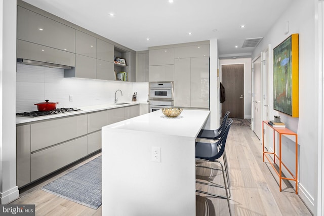 kitchen featuring light wood-type flooring, gray cabinets, a center island, appliances with stainless steel finishes, and a kitchen bar