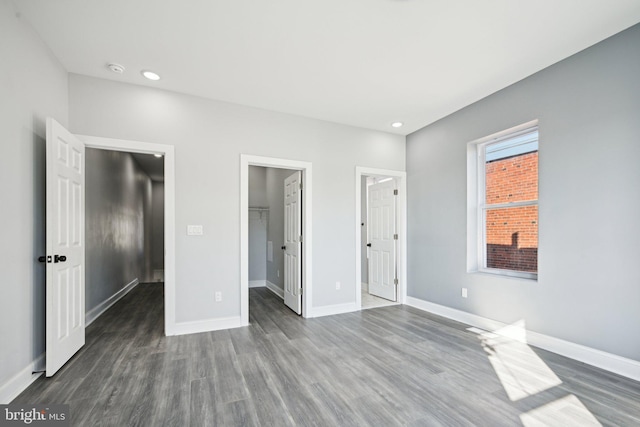 unfurnished bedroom with a spacious closet, dark wood-type flooring, and a closet