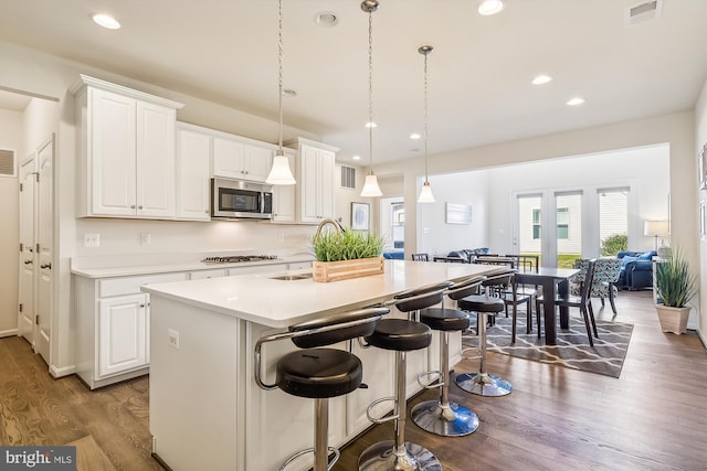 kitchen with an island with sink, stainless steel appliances, hardwood / wood-style floors, pendant lighting, and white cabinets