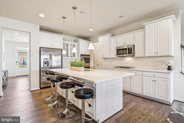 kitchen with appliances with stainless steel finishes, white cabinetry, dark hardwood / wood-style floors, and an island with sink