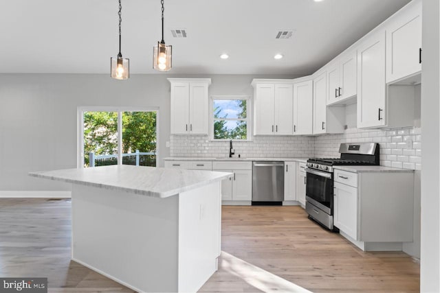 kitchen featuring appliances with stainless steel finishes, white cabinetry, a wealth of natural light, and pendant lighting